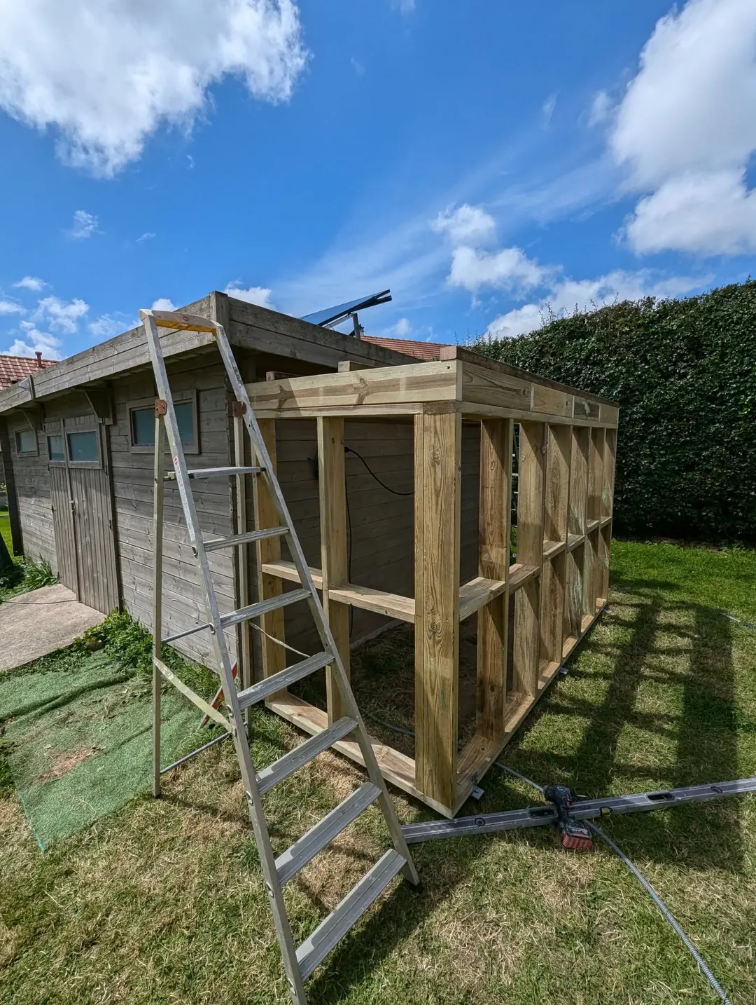 Ossature en bois d'un abri de jardin en construction, échelle appuyée contre la structure.
