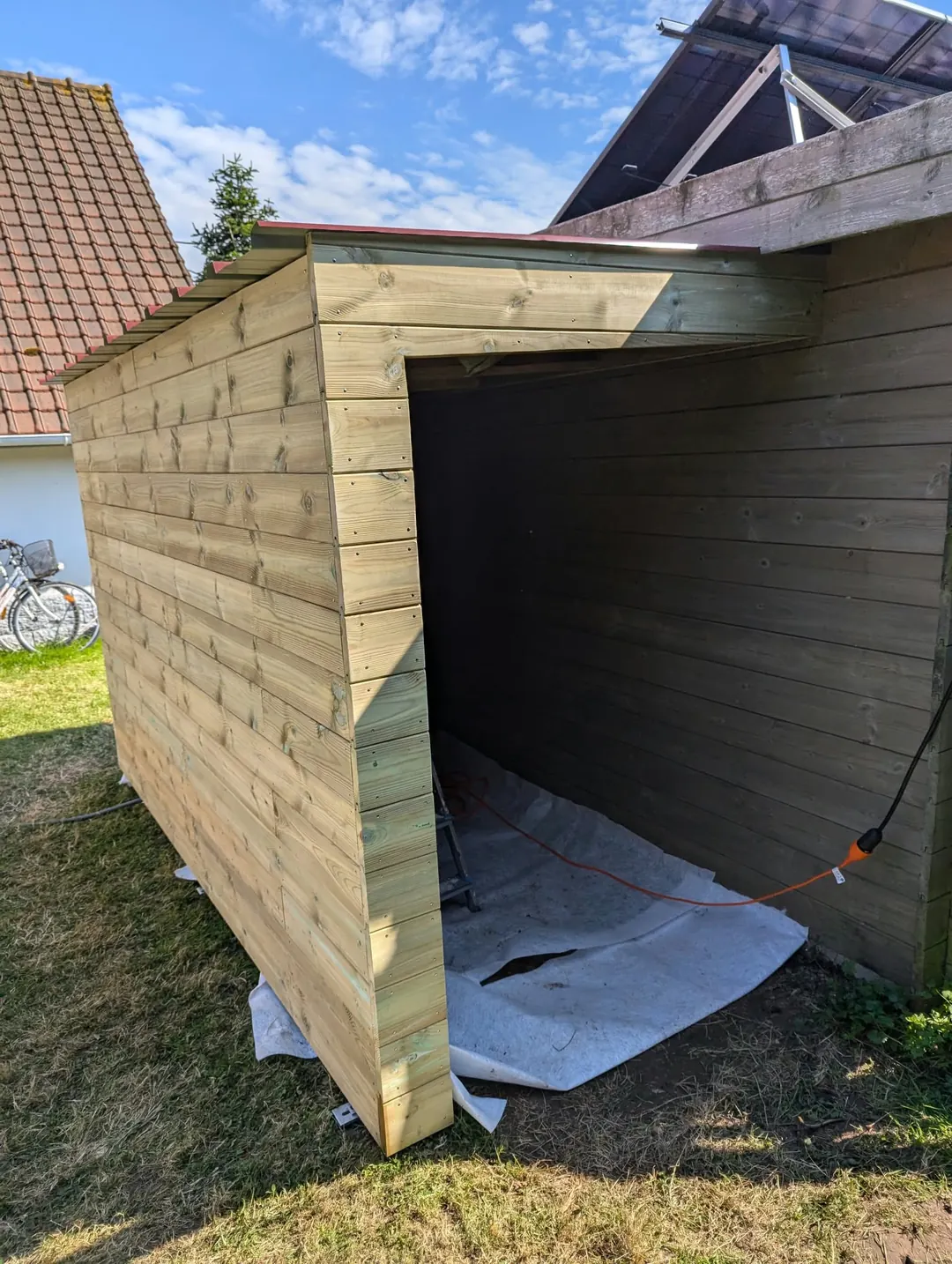 Abri de jardin ouvert sur un côté, bardage bois horizontal, bâche au sol.
