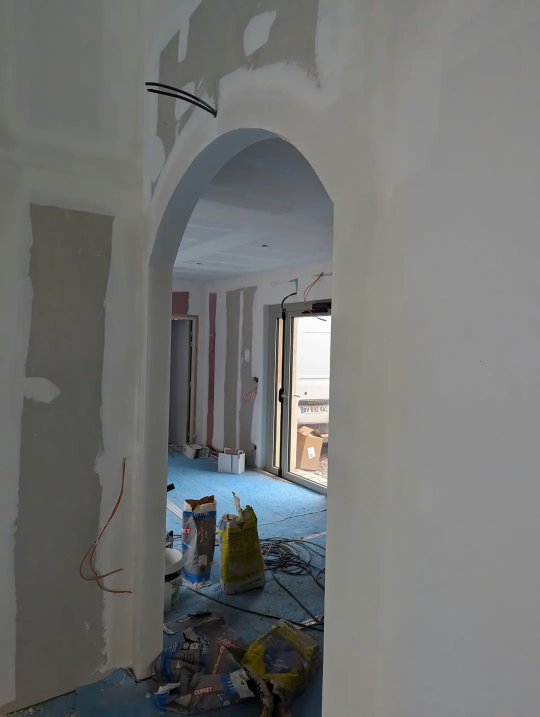 Passage en arche arrondie réalisé en plaque de plâtre, enduit de joints en cours, sacs d'enduit au sol.