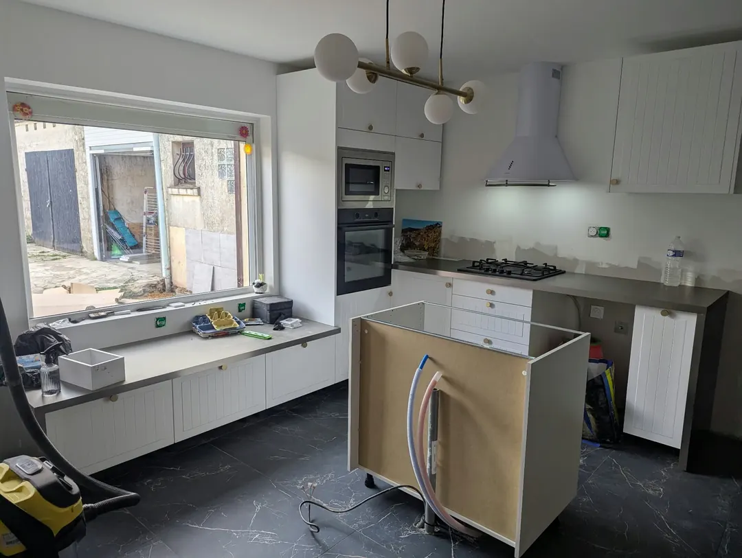 Cuisine en cours de montage : meubles blancs à façades moulurées, hotte, îlot sans façade au centre.