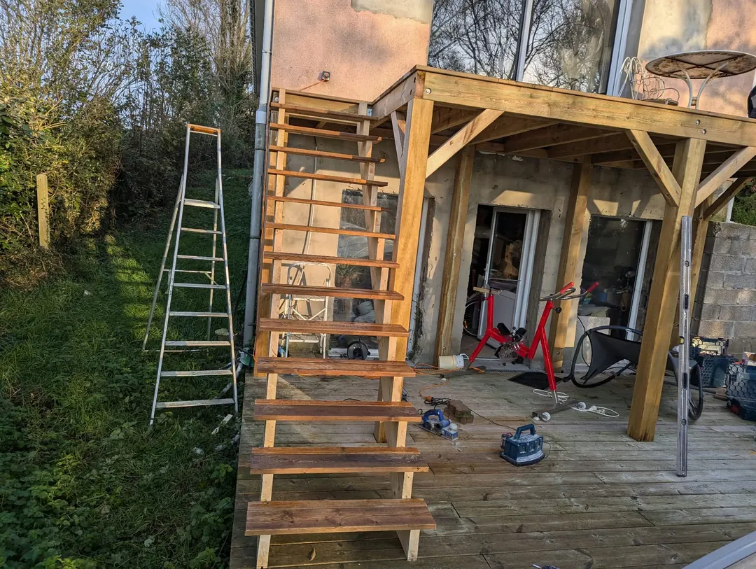 Escalier extérieur en bois descendant d'une terrasse vers le jardin, pergola au-dessus.