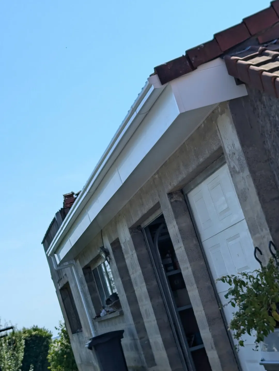 Bas de toit habillé : bandeau et sous-face blancs sous des tuiles rouges, façade en blocs béton.