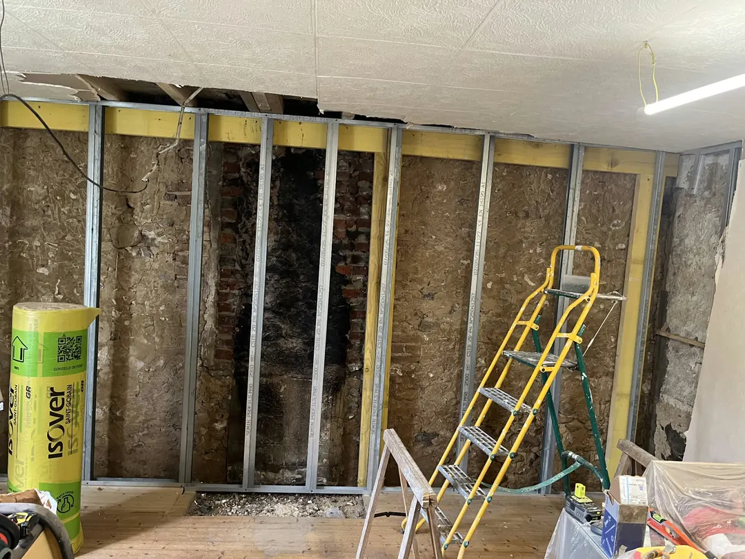 Montants métalliques verticaux posés devant un mur ancien, rouleau de laine de verre Isover au premier plan.