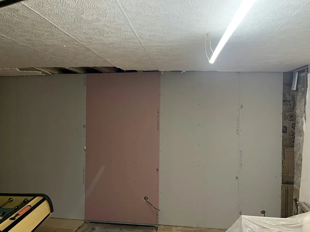 Le même mur fermé par des plaques de plâtre grises, avec une plaque rose au centre.
