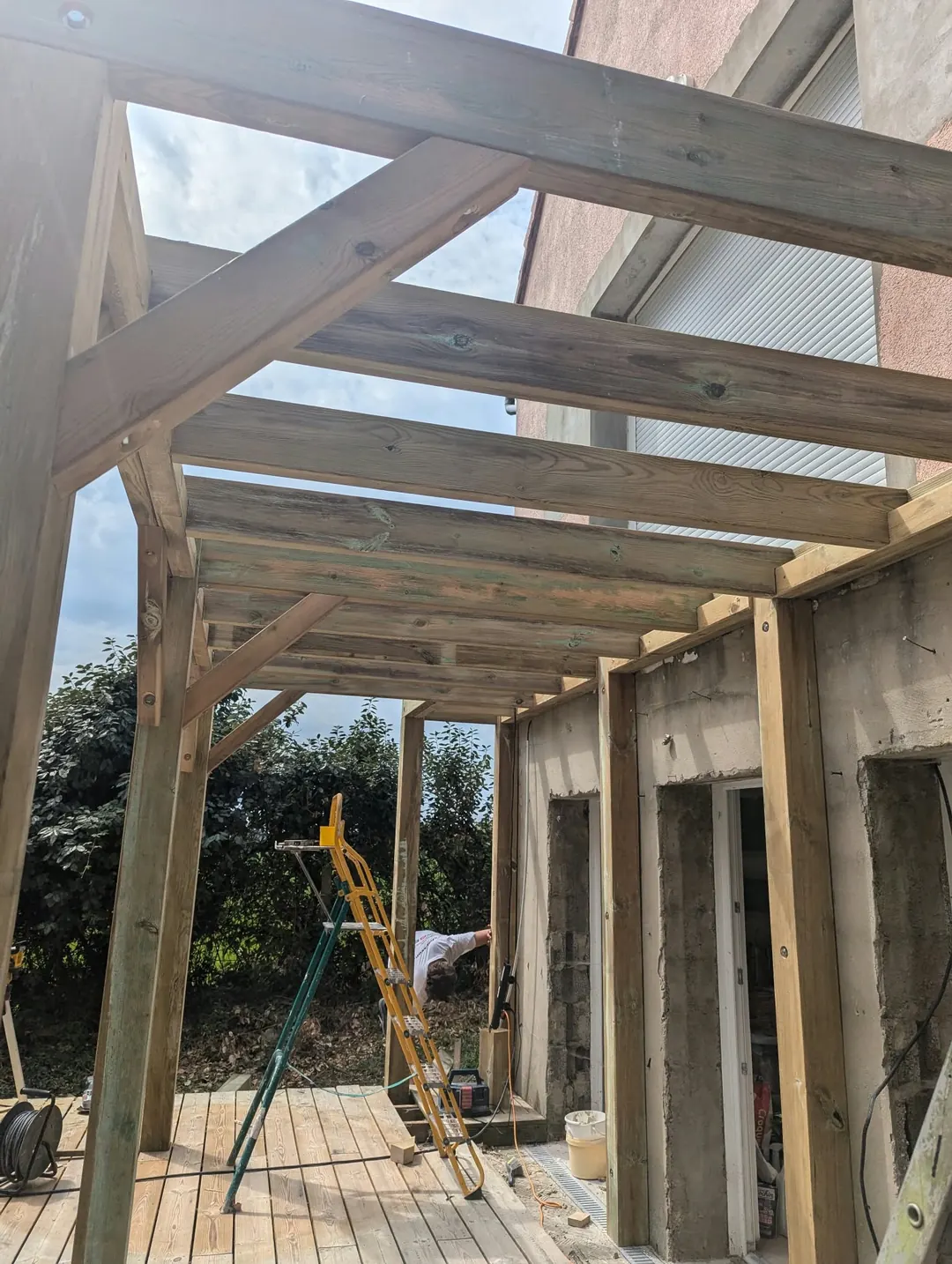 Pergola en bois vue d'en dessous : poutres, chevrons et jambes de force contre le ciel.