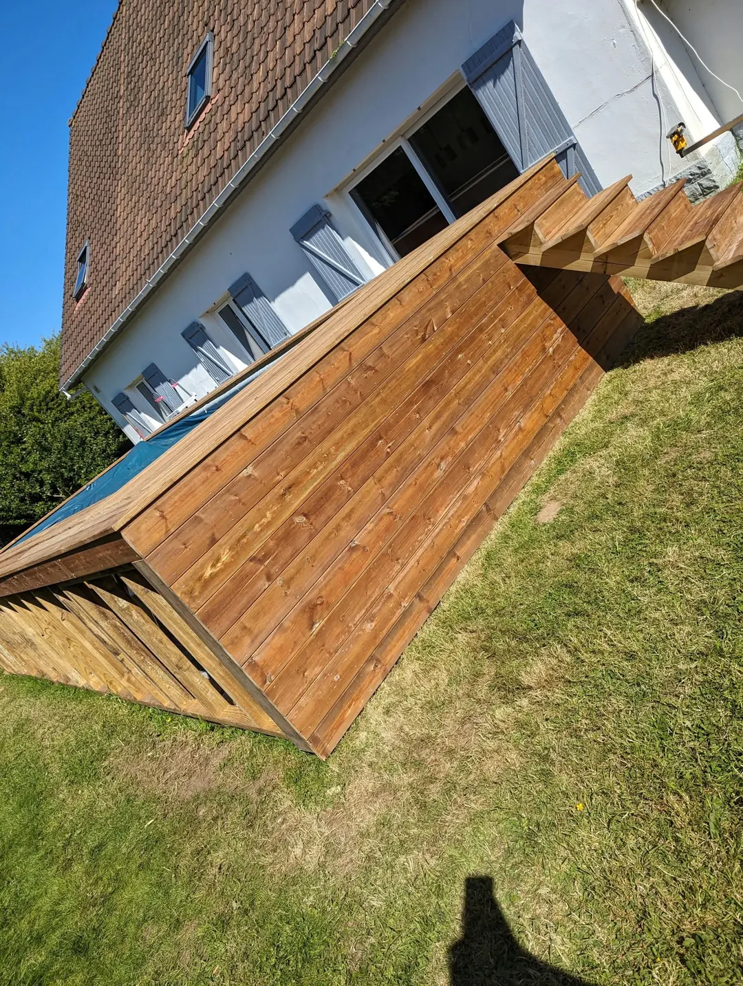 Piscine habillée de bois au pied d'une maison, escalier en bois à l'extrémité.