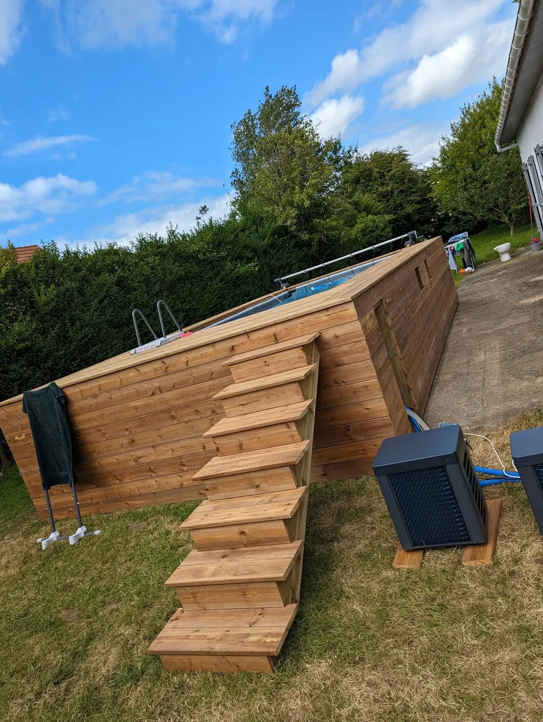 Piscine hors-sol entièrement habillée de lames de bois, escalier en bois pour y accéder.