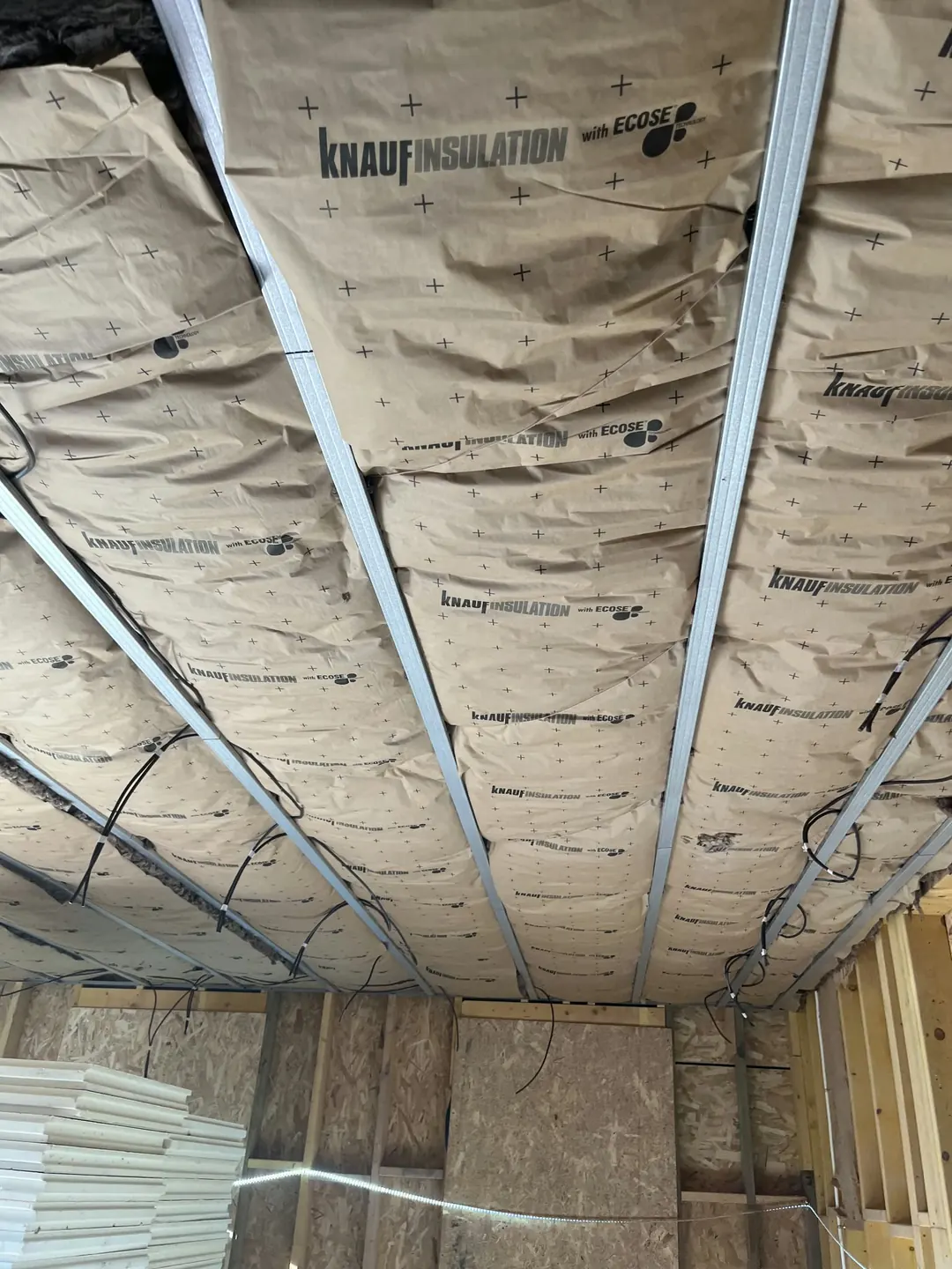 Plafond garni de laine de verre Knauf Insulation maintenue par des fourrures métalliques, murs en panneaux de bois.
