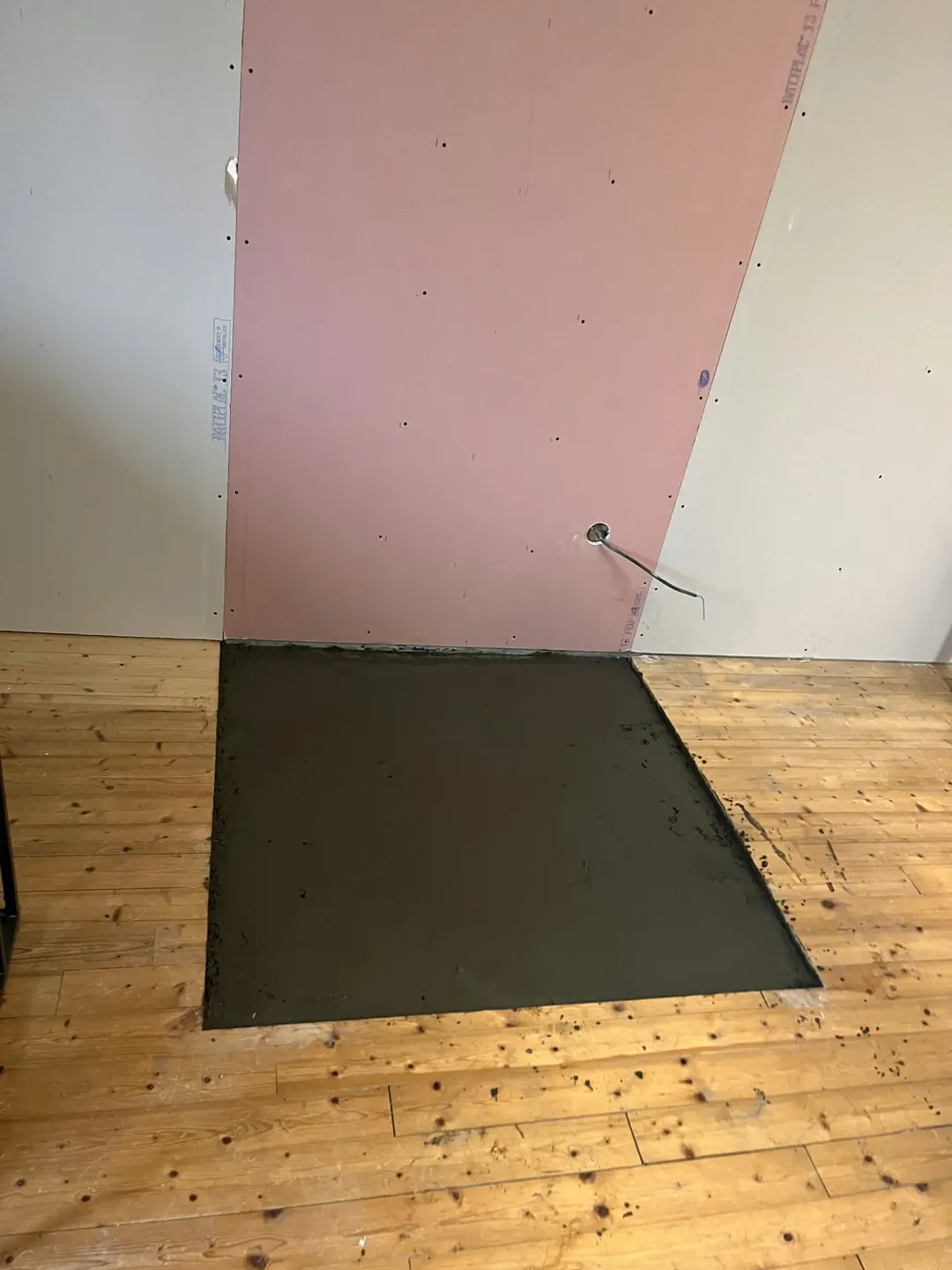 Plaque de plâtre rose posée entre deux plaques grises, carré de mortier frais dans un plancher en pin.